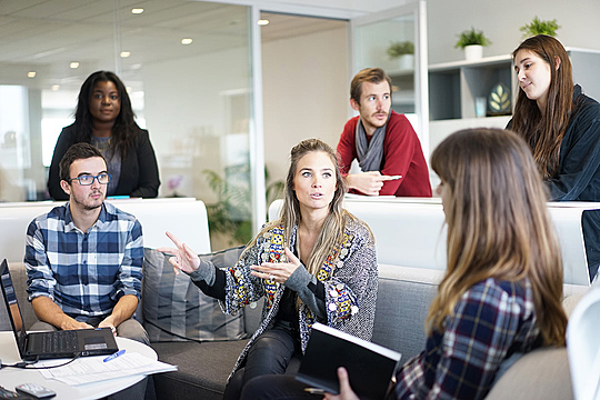 A group of people sitting and standing in an office working collaboratively together